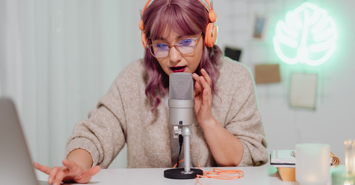 A young woman recording a podcast indoors with a microphone and headset, focused and engaged.