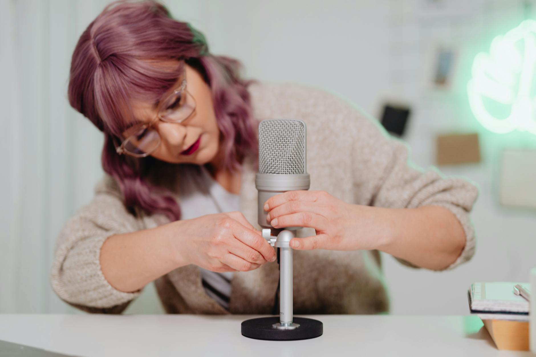 Woman with dyed hair adjusts a microphone in a cozy indoor setting, creating a relaxed atmosphere.