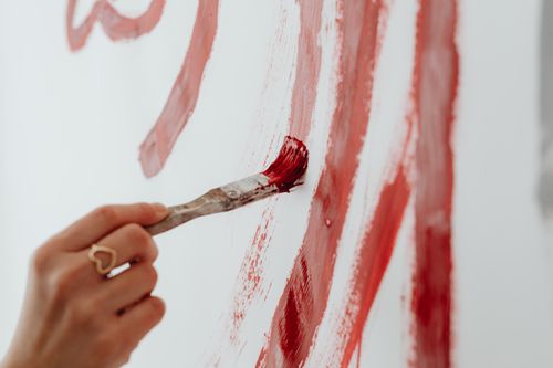 Free Close-up of a hand painting red brushstrokes on a white canvas, showcasing artistic creativity. Stock Photo