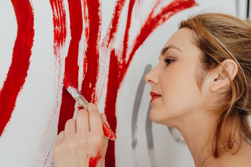 Free Close-up of a woman painting expressive red strokes on a canvas with a focused expression. Stock Photo