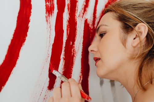 Free Close-up of a woman artist passionately painting red strokes on a canvas. Stock Photo