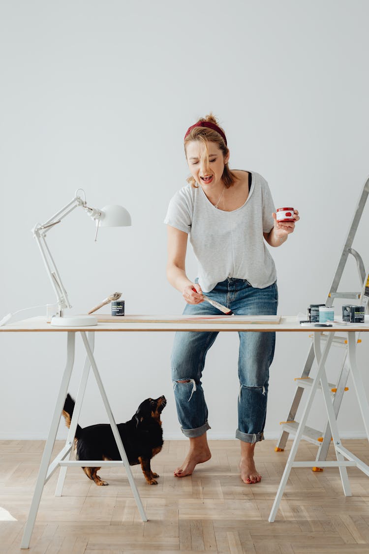 Woman Standing Behind A Desk And Singing While Painting