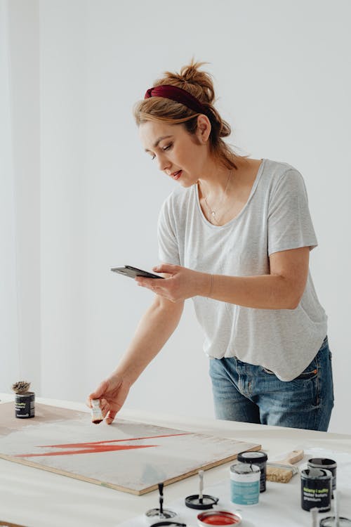 Photo of a Woman Painting while Looking at Her Cell Phone