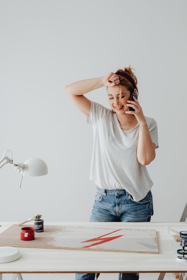 Woman Talking On The Phone And Looking At A Painting On The Table