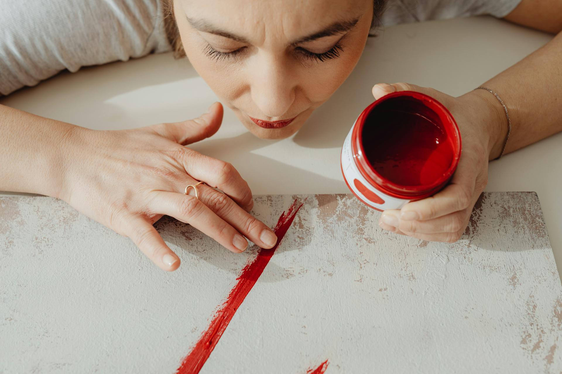 A woman artist uses her fingers to apply red paint on a canvas, showcasing creativity.