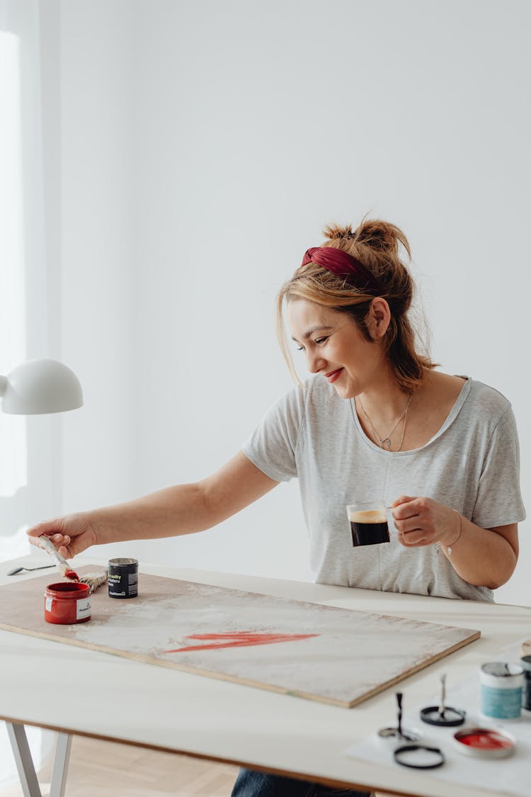 Woman Smiling While Painting And Drinking Coffee