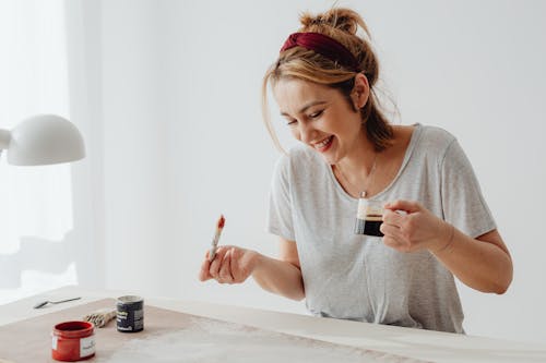 Photo of a Woman Holding a Paintbrush and a Cup of Coffee