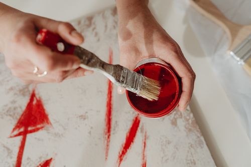 Free Close-up of hands dipping a paintbrush into red paint, creating abstract designs. Stock Photo