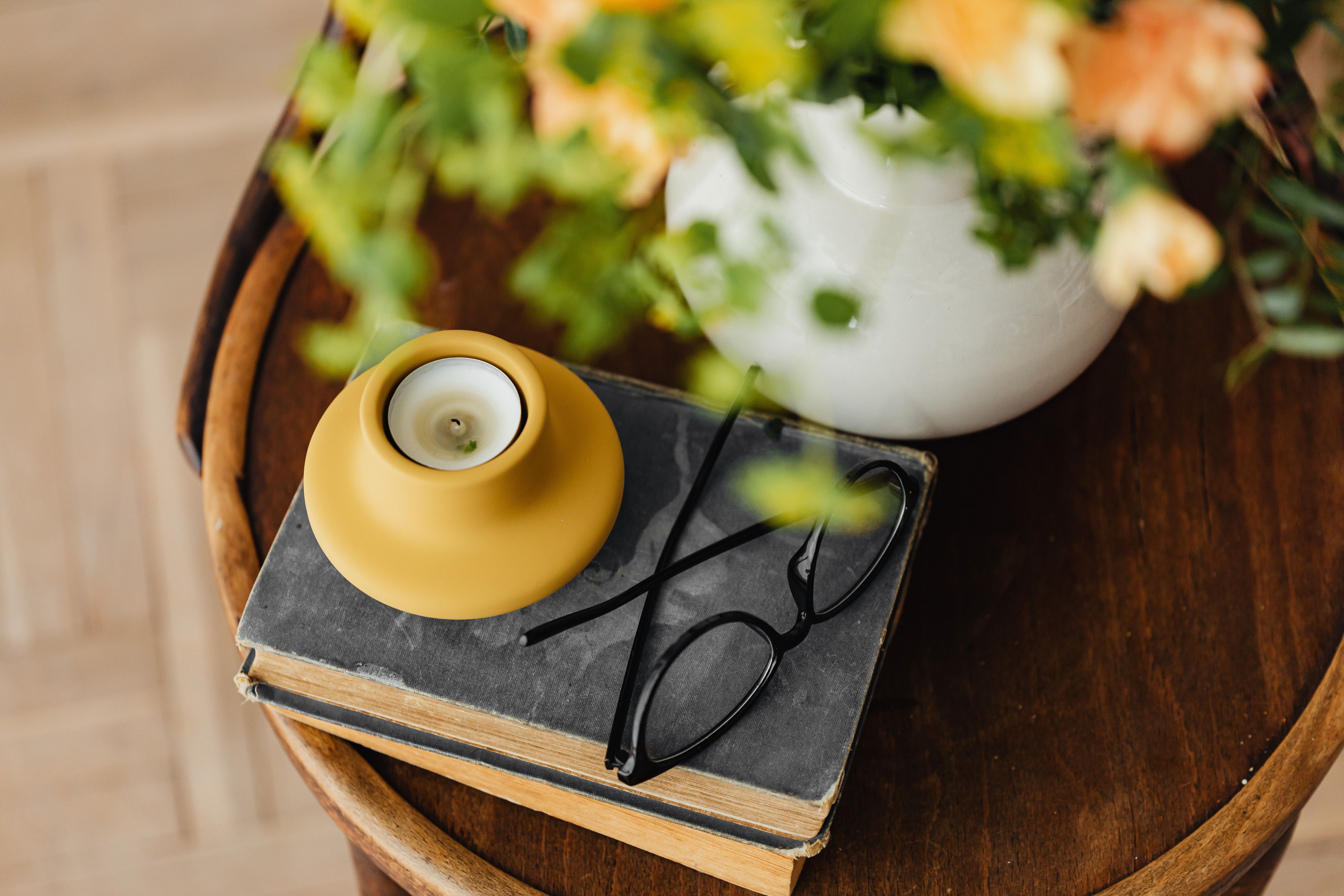 Vintage books, a candle, and glasses create a cozy still life scene with floral decor.