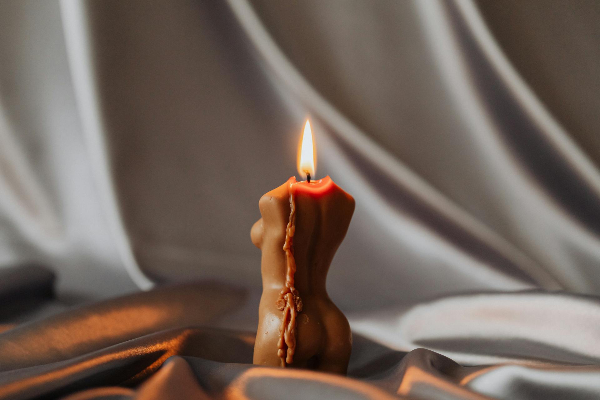 A romantic scene showcasing a body-shaped candle burning on luxurious silk fabric.