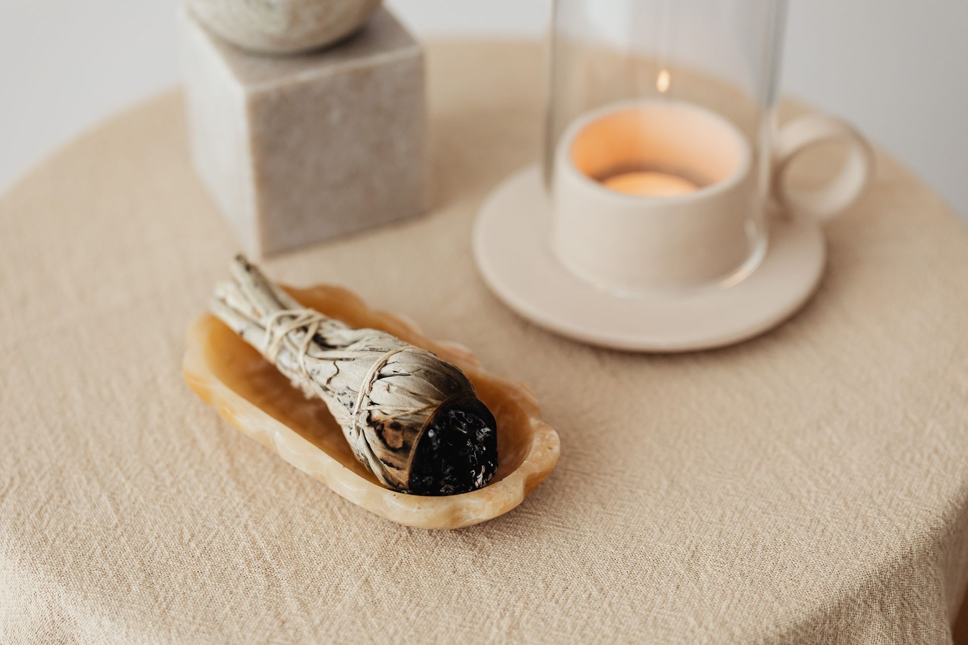A peaceful aromatherapy scene featuring a burning candle and sage on a beige tablecloth.