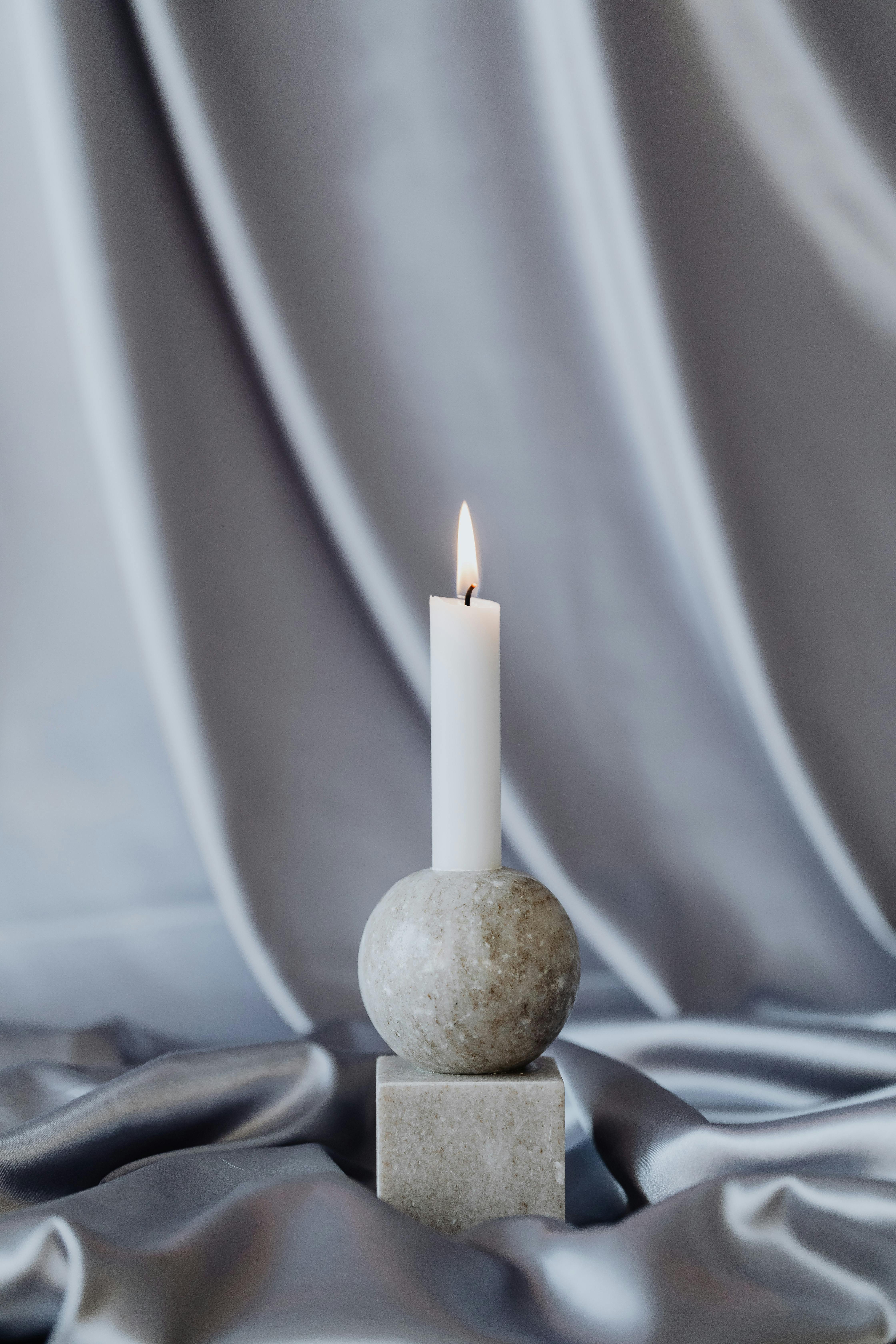 A minimalist candle on a stone base with elegant silk drapery background.