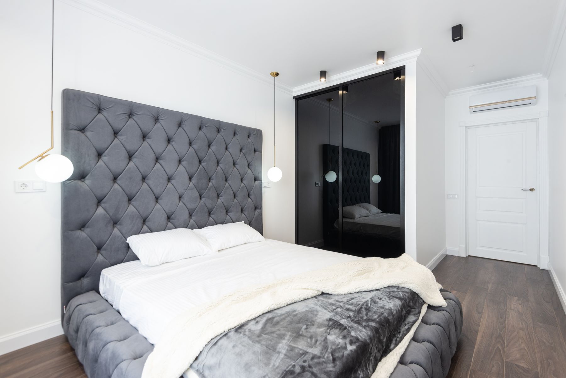 Gray tufted upholstered bed with white bedding and a pale throw in a room with white walls and dark timber flooring