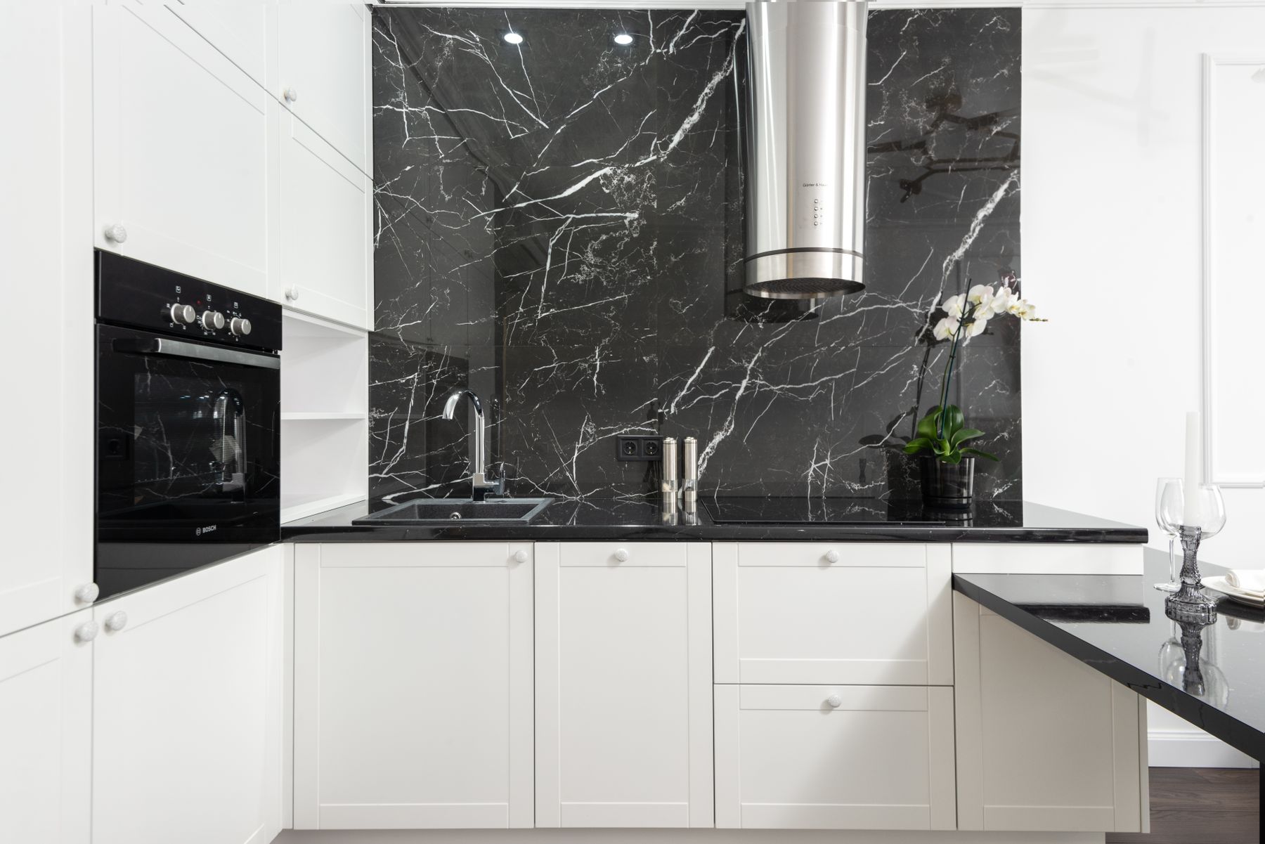 White kitchen cabinetry framing a large black marble backsplash with veining