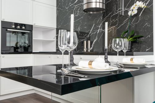 Free Empty goblets with candlesticks served on black table near plates with rolled napkins in creative kitchen with white cupboards and modern appliances Stock Photo