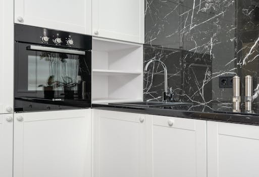 Sleek kitchen featuring a black marble backsplash, white cabinets, and a contemporary oven.