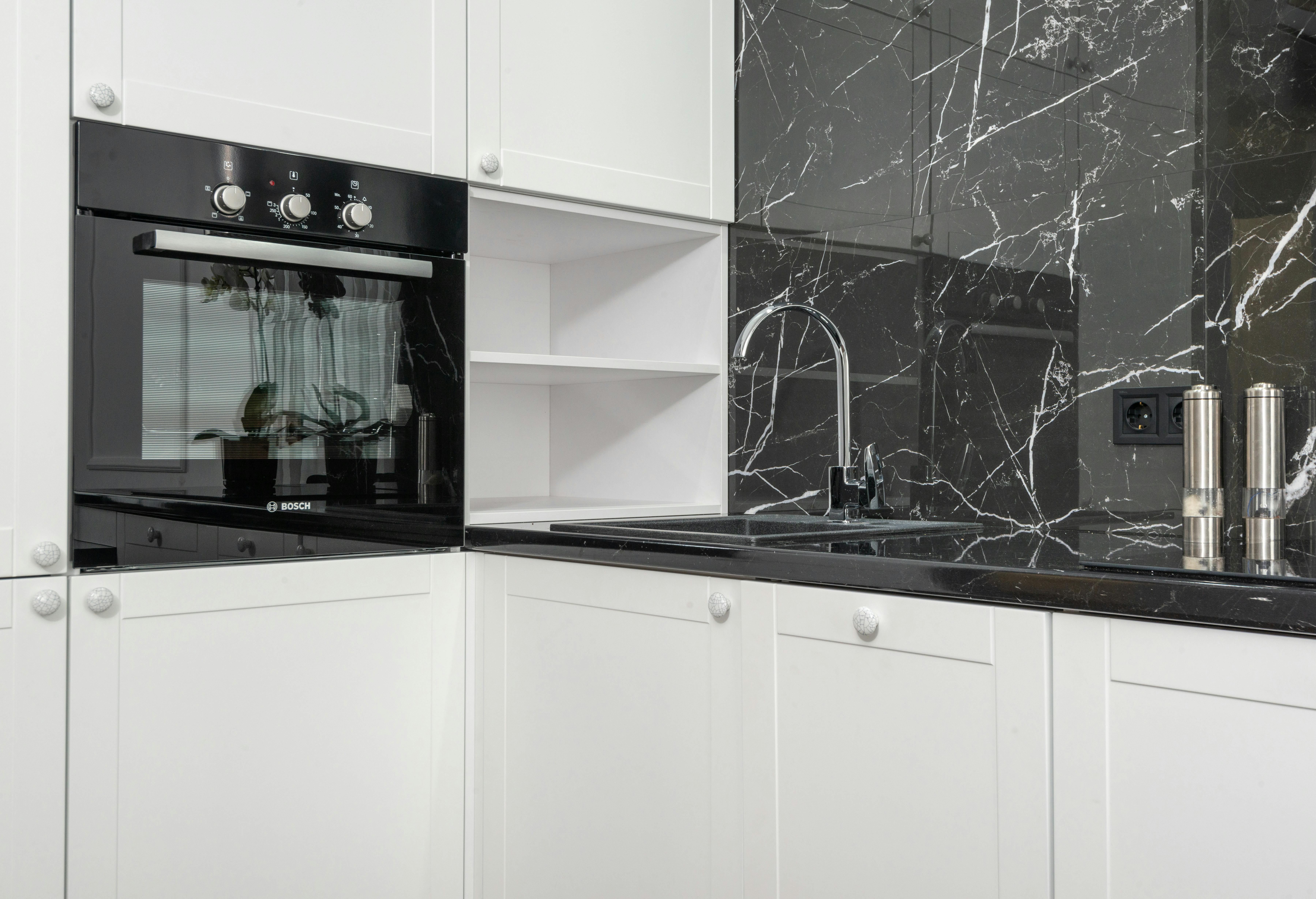 Modern kitchen is white with a black marble countertop. Stove, oven,  cabinets and sink with tap Stock Photo - Alamy