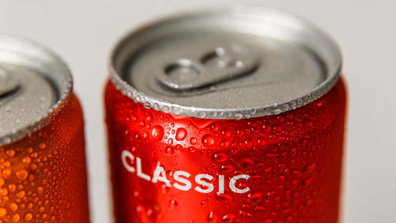 Refreshing close-up of wet red and orange soda cans with condensation droplets.
