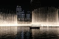 夜晚，船的剪影映衬着被照亮的迪拜喷泉，展现出城市的地平线