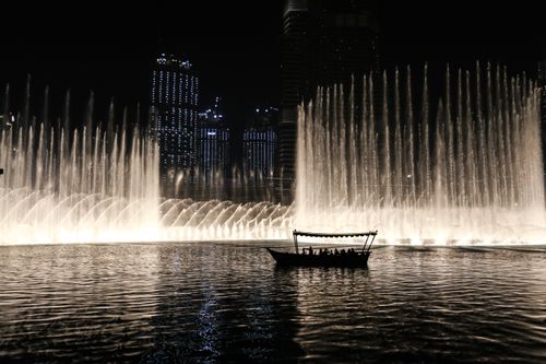 Free Silhouette of a boat against the illuminated Dubai Fountain at night, showcasing the city skyline. Stock Photo