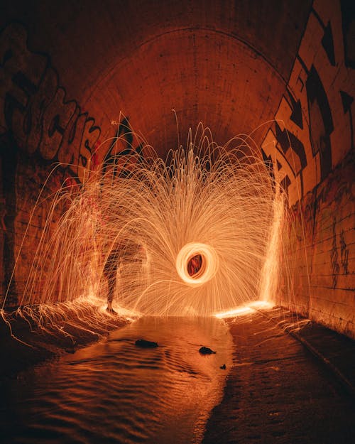 Side view of unrecognizable person in glowing freeze light with curved beams in sewer tunnel with graffiti walls at night