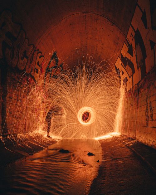 Free Side view of unrecognizable person in glowing freeze light with curved beams in sewer tunnel with graffiti walls at night Stock Photo