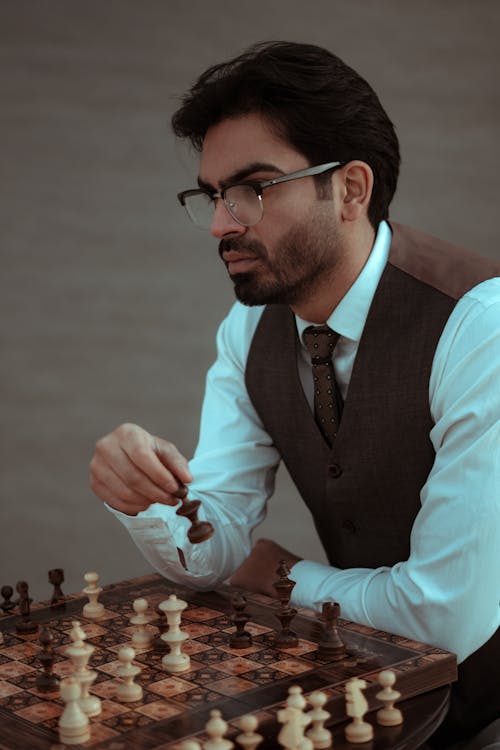 Contemplative bearded male in classy suit and eyeglasses playing chess during competition in studio