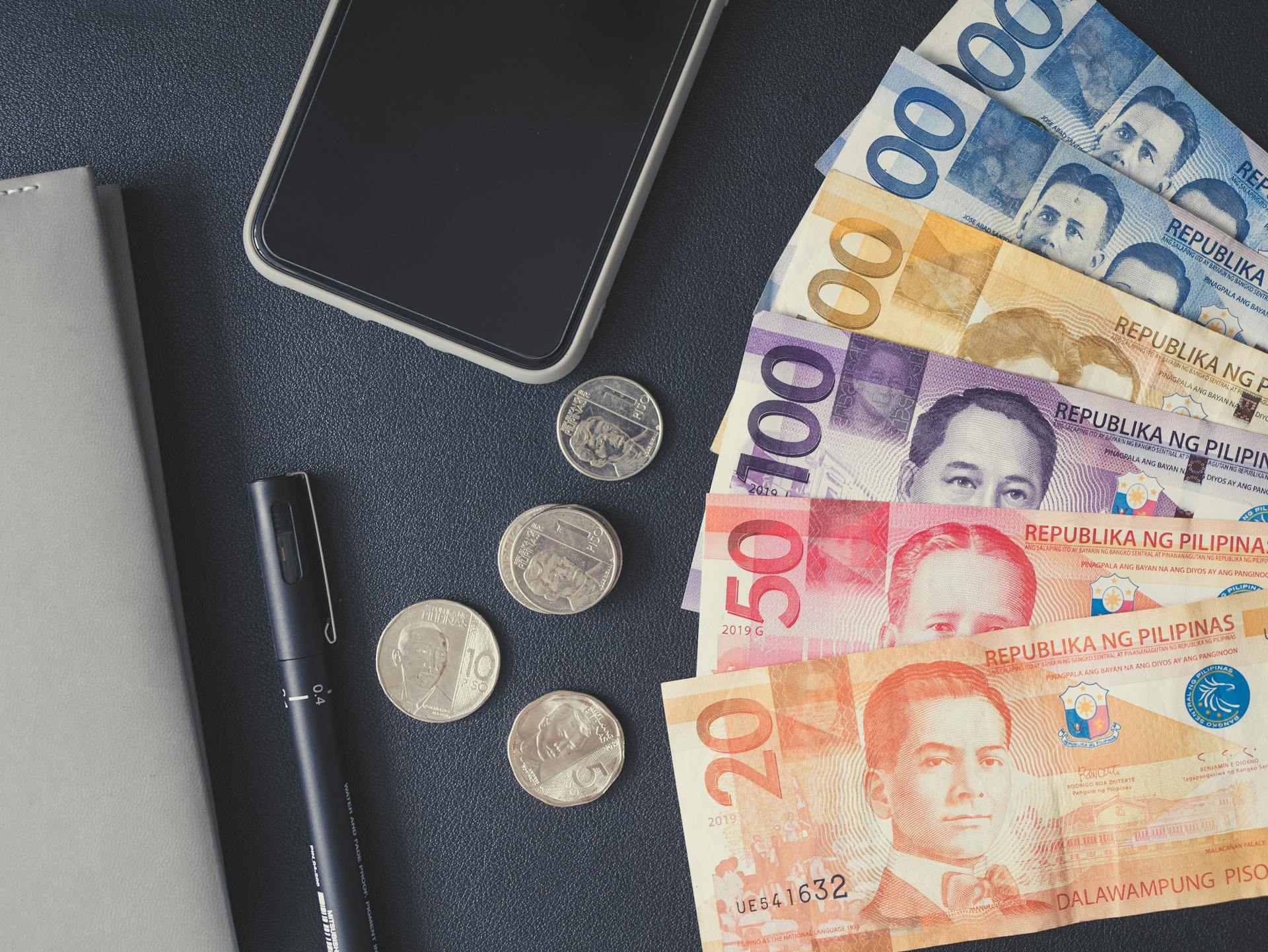 Flat lay of Philippine peso bills, coins, smartphone, and notebook. Ideal for financial themes.