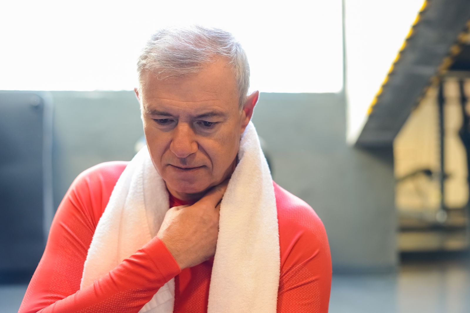 Older adult resting with a towel between strength-training sets in a gym.