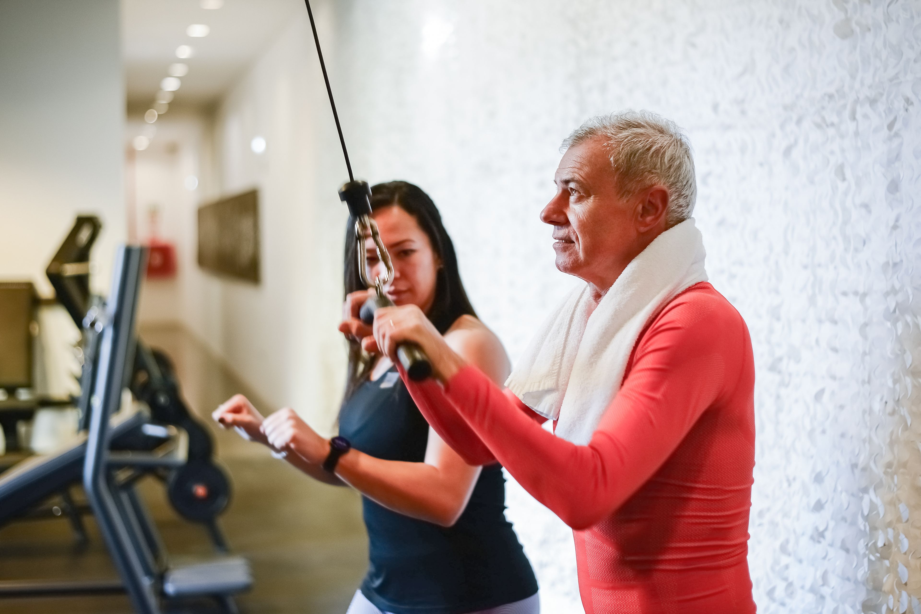 A senior man exercises with a personal trainer in the gym, promoting health and fitness.
