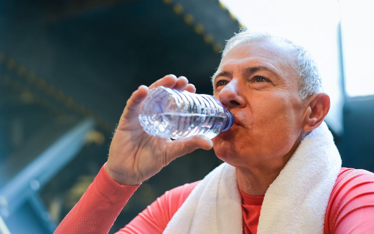 Elderly man drinking water post-exercise with towel around neck, promoting healthy lifestyle.