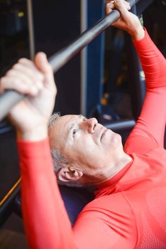Elderly man lifting barbell in gym promotes healthy lifestyle and strength.