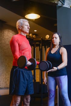 Elderly man doing dumbbell curls with a personal trainer guidance.