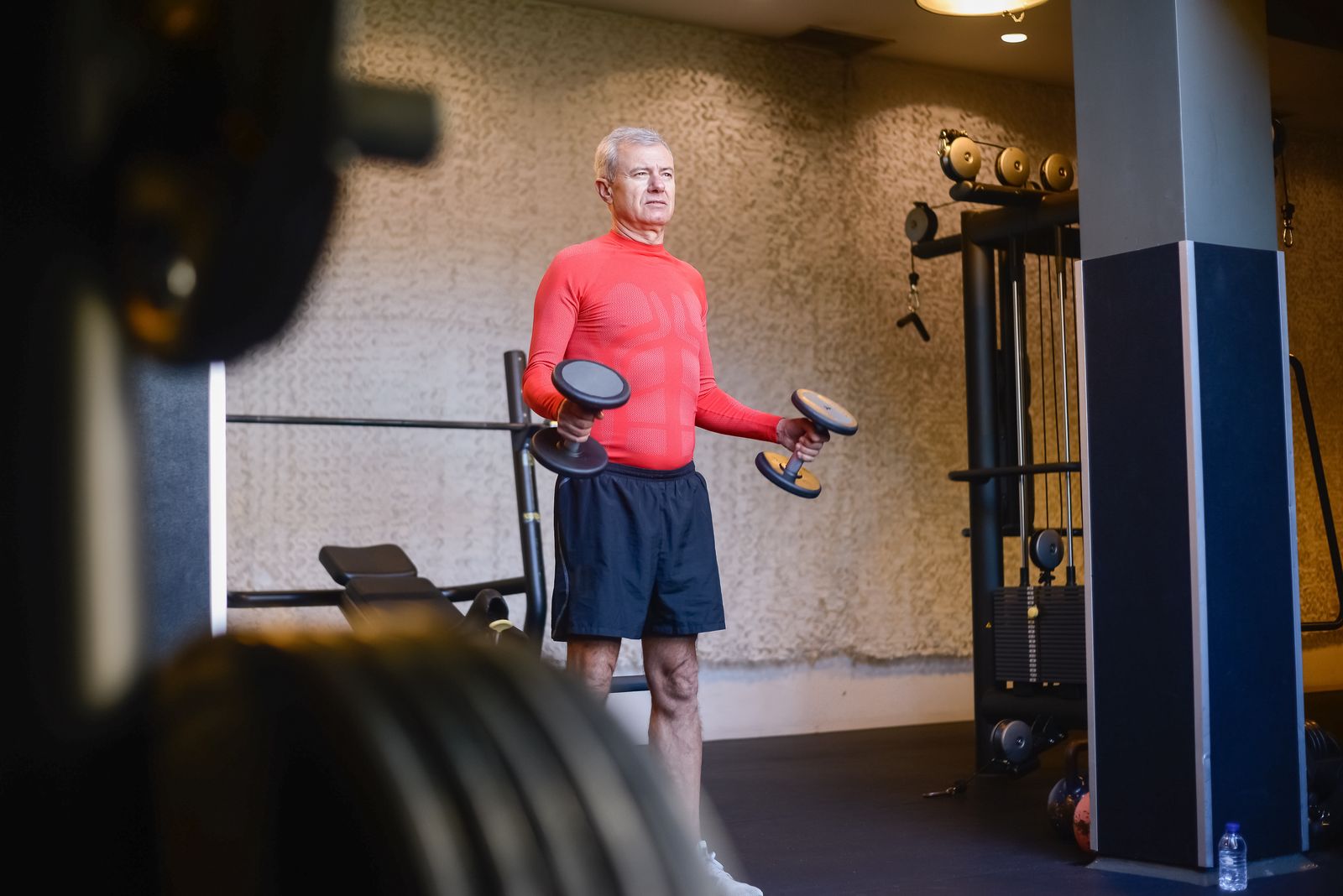 Older man lifting dumbbells in a gym.