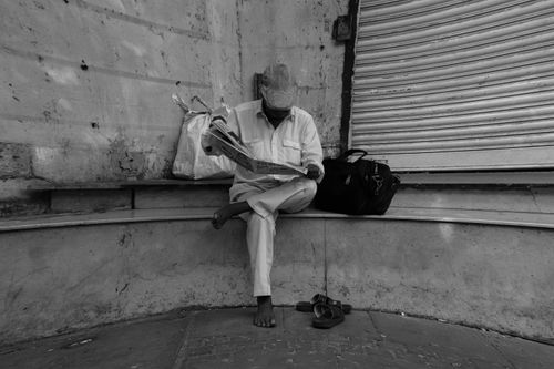 Free A man sits on a bench in Mumbai, engrossed in reading a newspaper. Monochrome tone. Stock Photo