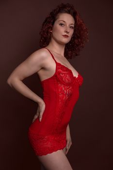 Studio portrait of a woman posing confidently in red lingerie against a dark backdrop.