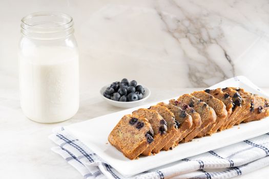 Sliced blueberry bread with a jar of milk and fresh blueberries on a white plate.