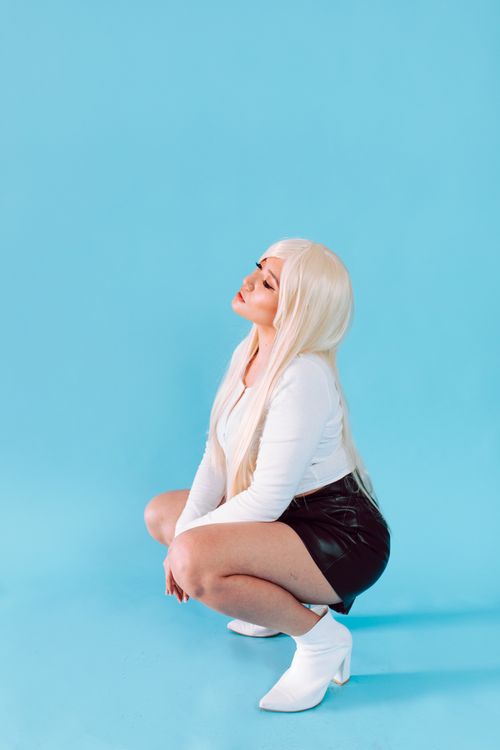 Free Stylish woman with blonde hair posing against a bright blue background, wearing a leather skirt and white boots. Stock Photo