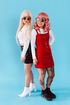 Two stylish women in trendy wigs and fashionable outfits posing against a blue background.
