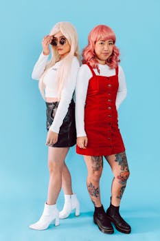 Two stylish women with colorful wigs and tattoos, posing confidently in trendy outfits.