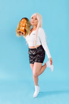 Stylish woman in black leather shorts displays a blonde wig on a mannequin head.