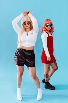 Two young women posing in trendy outfits with sunglasses and vibrant hairstyles.
