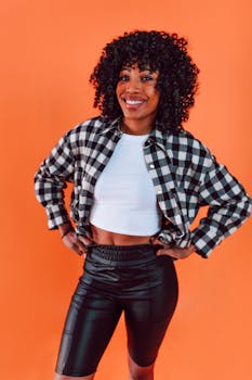Portrait of a smiling woman in trendy attire, posing against an orange backdrop with confidence and style.