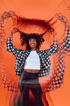 Capture of a joyful young woman with curly hair in a dynamic, stylish pose against an orange background.