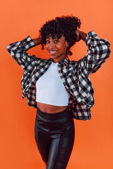 Portrait of a stylish woman with curly hair against a bright orange background.