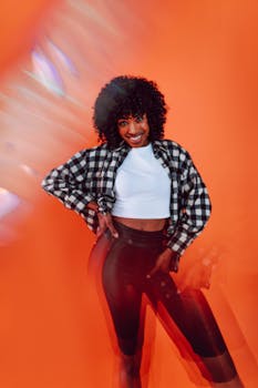 Smiling woman with curly hair poses confidently against an orange background.