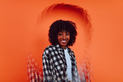 Portrait of a woman with curly hair and checkered shirt against an artistic orange backdrop.
