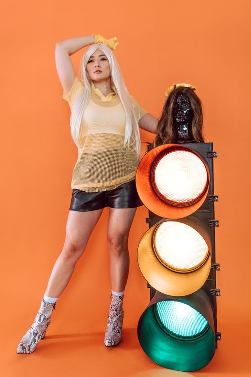 Free Stylish woman in studio with orange backdrop, dressed in yellow, posing with traffic light. Stock Photo