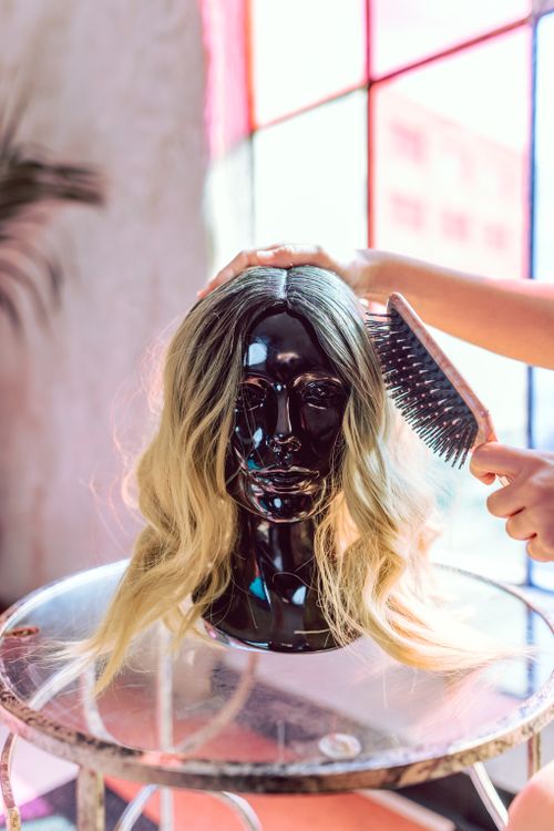 Free A fashionable blonde wig being styled on a black mannequin head indoors. Stock Photo