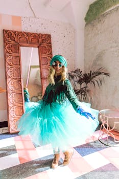 Stylish woman in a green tulle dress and sunglasses posing indoors with a mirror.